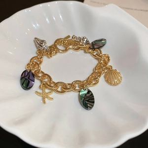 Golden ocean theme bracelet with seashell and starfish charms on a white ceramic shell tray
