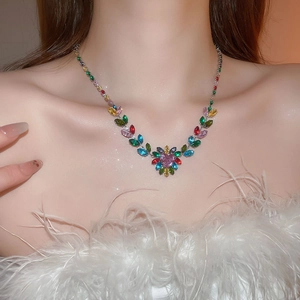 Macro view of crystal heart pendant and multi-colored gemstone leaf necklace on model