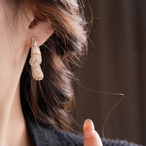 Detailed close-up of zircon teardrop earrings in golden finish on a model's ear
