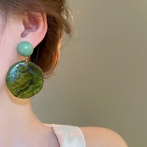 Detail of green resin earrings with marbled texture worn by a model in a profile view