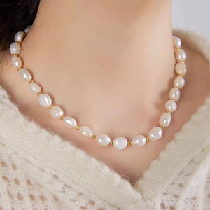 Detailed view of white baroque pearl necklace with golden beads on a model neckline
