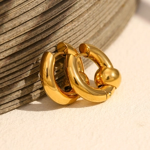 Close-up of chunky gold beaded hoop earrings on a textured wooden ring background