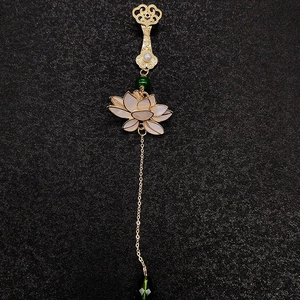 Détail de broche chinoise dorée avec lotus blanc, perles et pompons verts sur fond noir