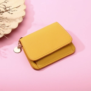 Close-up of yellow leather wallet with pebble grain texture and round metal charm