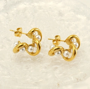 Macro detail of wave-shaped 18K gold earrings with white pearls on a frosted glass surface