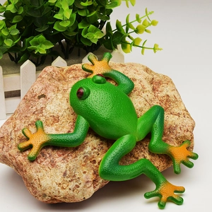 Realistic green rubber frog model with orange gradient limbs resting on a natural stone