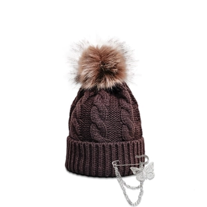 Close-up of cable knit beanie with faux fur pompom and butterfly pin with metal chains