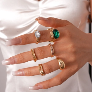 Close-up of vintage gold rings set featuring emerald and pink gems on white fabric