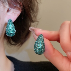 Detailed macro view of luxury emerald zircon drop earrings being held and worn on ear