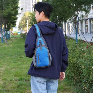 Blue waterproof outdoor chest bag with grey trim worn by a model in a park setting