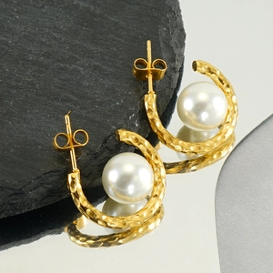 Detailed shot of C-shaped hammered gold earring with large white pearl on slate base