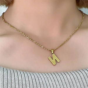 Primo piano di una collana con ciondolo a lettera N in acciaio dorato su modella