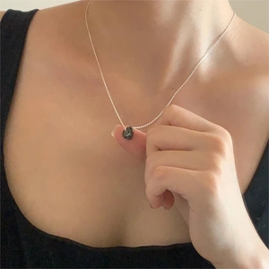 Close-up of minimalist silver chain with an irregular black stone pendant on a model