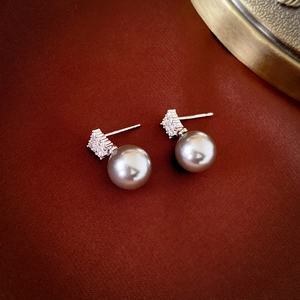 Macro shot of silver-tone faux pearl earrings with square cubic zirconia studs on leather