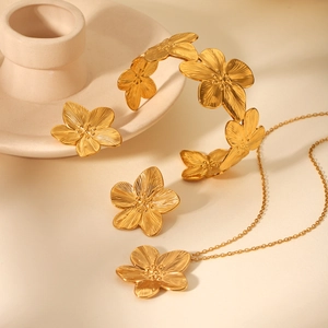 Detailed set of 18K gold plated stainless steel textured flower jewelry on beige background