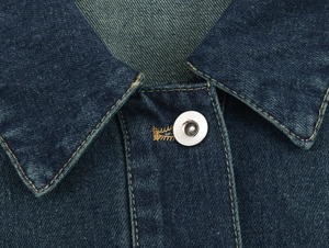 Détail du col d'une veste en jean bleu foncé avec coutures et bouton en métal argenté