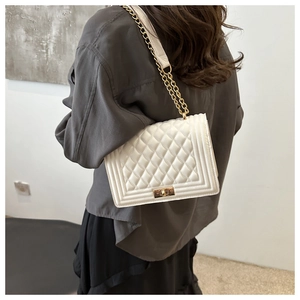 Detailed view of a white quilted shoulder bag with gold chain strap on a model