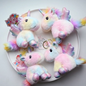 Set of four rainbow plush unicorn keychains with iridescent wings on a white tray
