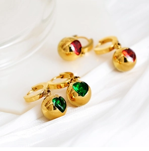 Détail de boucles d'oreilles dorées avec pierres de zircon en forme de cœur vertes et rouges
