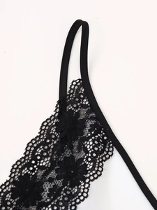 Dettaglio del pizzo floreale nero cucito su tessuto bianco con spalline sottili