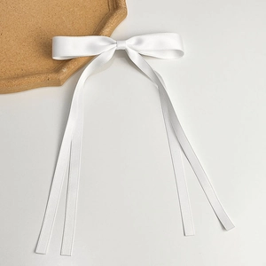 Detailed close-up of white satin bow hair clip with long ribbons on minimalist background