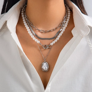 Detailed view of layered baroque pearl and silver snake chain necklaces on model