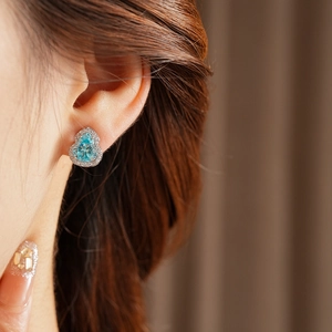 Close-up of a pear-shaped light blue gemstone earring with zircon halo on a model's ear