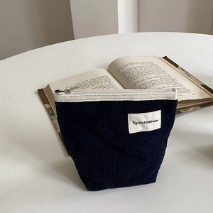 Navy blue corduroy cosmetic bag with zipper and logo label on a white table