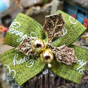 Close-up of green fabric holiday bow with Happy Holidays text and golden holly leaf detail