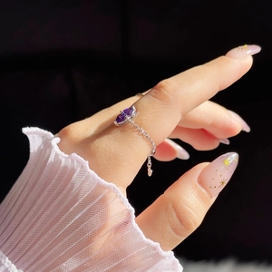 Close-up of a silver chain ring with a purple pear-shaped gemstone on model's hand