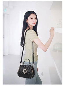 Detail of black pleated bucket bag with gold crown heart buckle on model with green top