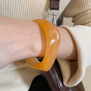 Close-up of a wide orange acrylic bracelet with a glossy finish on a model wrist