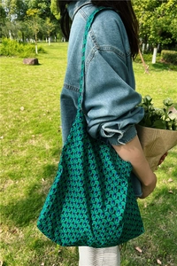 Close-up of green and blue geometric pattern tote bag worn with a casual denim jacket