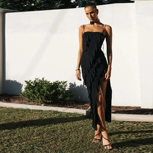 Détail d'une robe noire dos nu avec volants et fente sur fond de pelouse extérieure