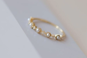 Detail shot of a slender gold ring featuring alternating small white pearls and crystals