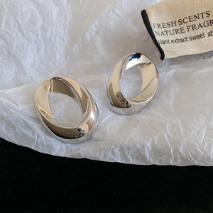 Macro shot of polished silver oval twisted hoop earrings on white textured paper background