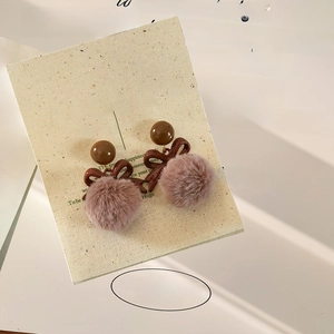 Close-up of bow earrings with brown beads and pink pom poms on a textured vintage background