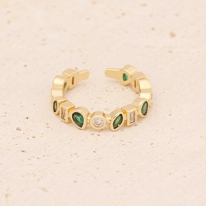 Detailed close-up of golden open ring featuring green and white zircon stones on sand