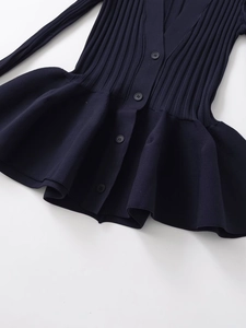 Detail of dark blue knit top featuring vertical ribbing, buttons and ruffle hem