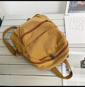 Detailansicht eines senfgelben Canvas-Rucksacks auf Metalltisch mit Laptop