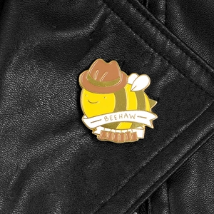 Détail du badge abeille en émail avec chapeau de cowboy et bottes sur cuir noir