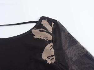 Detail van beige bloemenborduursel op zwarte mesh mouwen van een sexy jurk