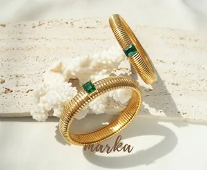 Detail of gold-plated bracelets with textured patterns and rectangular green zircon inlay