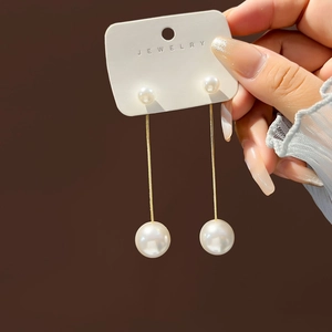 Detail of long gold chain earrings featuring double pearls and star stud accents