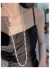 Gros plan d'un long collier de perles blanches porté avec une robe élégante en satin