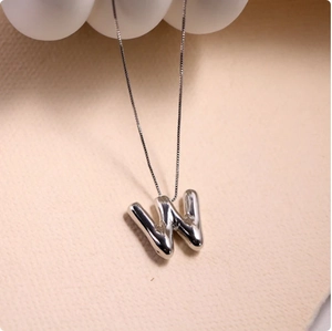 Detailed macro view of 3D balloon letter W pendant with polished silver finish on box chain