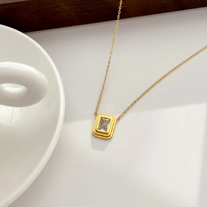 Close-up of a gold rectangle zircon necklace on a wooden and ceramic lifestyle background