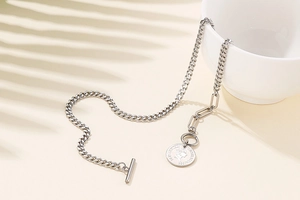 Detail of silver chain necklace with coin pendant and OT clasp on beige surface