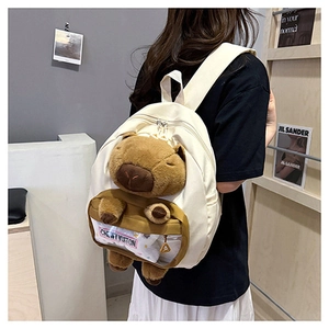 Detail showing white canvas backpack featuring a 3D plush capybara and transparent pocket