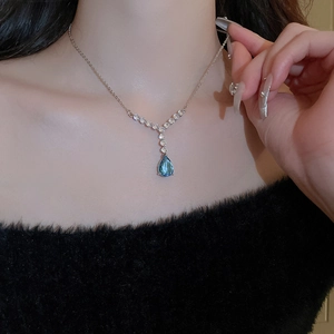 Gros plan d'un pendentif avec pierre bleue en poire sur chaîne en argent portée par un mannequin